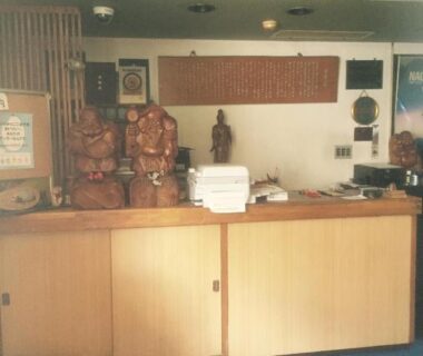 Reception area with wooden counter, decorative statues and slippers at Umeoka Ryokan in Nagano, Chubu