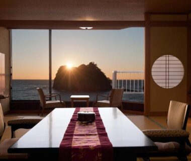 Tatami room with low table and shoji screens opening to a coastal sunset over rocky sea in Shizuoka