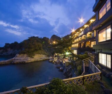 Ryokan exterior lit at dusk along rocky coast near UmibenokakureyuSEIRYU海辺のかくれ湯清流 in Shizuoka
