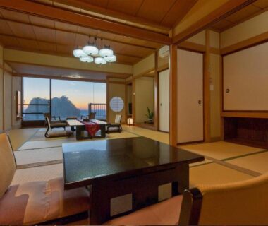 Tatami room with low table, chairs and sliding doors opening to coastal view at dusk