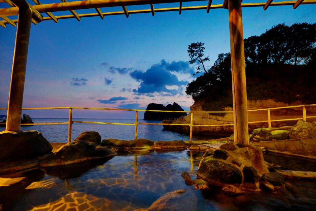 Seaside outdoor onsen UmibenokakureyuSEIRYU Shizuoka Outdoor stone onsen bath under wooden shelter overlooking calm sea at dusk, UmibenokakureyuSEIRYU, Shizuoka