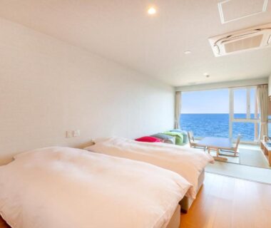 Twin beds and seating area with large window overlooking the ocean at Umino Hotel Hajime, Oita