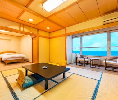 Spacious tatami room with low table, futon bedding and window overlooking sea at Umino Hotel Hajime, Ōita