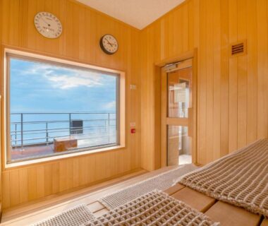 Wood-paneled relaxation room with reclined mats and window overlooking the sea at Umino Hotel Hajime, Ōita