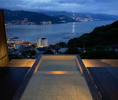 Stone outdoor onsen bath on terrace overlooking bay at dusk, Uminohana, Shizuoka, Chūbu