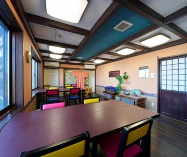 Interior dining room with wooden tables, colorful chairs, shoji door and large windows at Uminone in Hyōgo