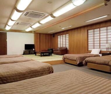 Large guest room with multiple beds, tatami flooring, shoji screens and low table at Uomisaki Hotel in Shizuoka