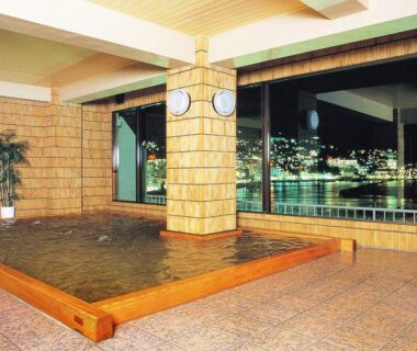 Indoor communal bath with large windows overlooking city lights at Uomisaki Hotel, Shizuoka