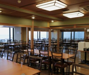 Large dining area with wooden tables and chairs overlooking coastal view at Uomisaki Hotel in Shizuoka