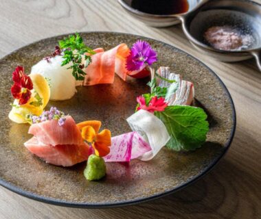 Artful sashimi arrangement with edible flowers, wasabi, and dipping sauces on a ceramic plate at Urakusatsu TOU