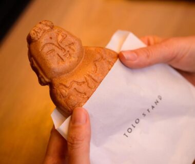 Hands holding a doll-shaped baked confection wrapped in Urakusatsu TOU paper at a Gunma ryokan