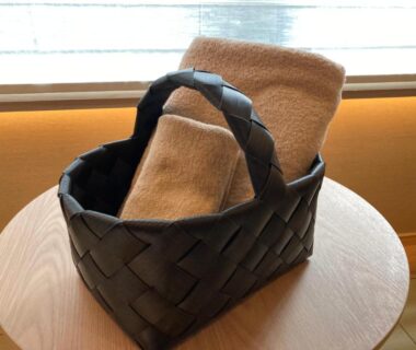 Woven black basket with folded towels on wooden table by window in ryokan room at Urakusatsu TOU, Gunma