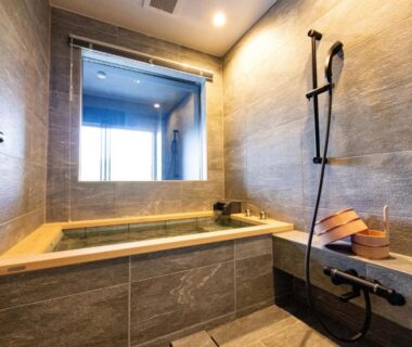 Indoor stone-tiled bathtub with hand shower and wooden bucket at Urari Takeo Garden Terrace Spa Resorts, Saga