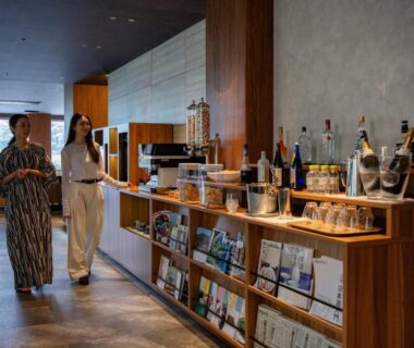 Two guests in yukata and casual wear in lounge by wooden bar, shelving, and large window