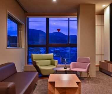 Modern lounge with sofa, armchairs and low table facing large window overlooking mountains and town lights