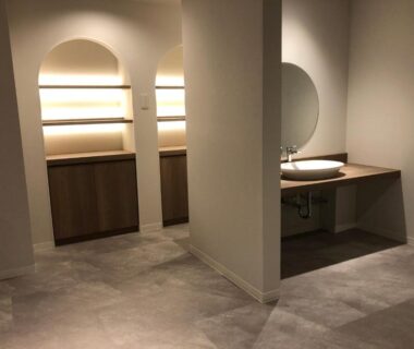 Neutral onsen dressing area with round mirror, sink and tiled floor at Ureshino Onsen Yusyuku Sarayama in Saga