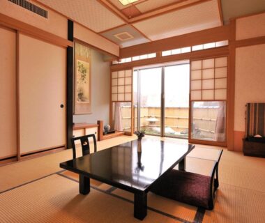 Tatami room with low lacquered table, zabuton cushions, shoji doors and tokonoma alcove at Uruoikan, Nagano