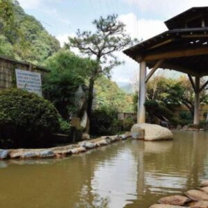 Covered outdoor onsen bath with stone edging and garden at Uruoikan in Nagano
