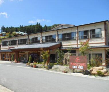 Two-story ryokan building with entrance and wooden sign, mountain backdrop in Ōita, Kyūshū