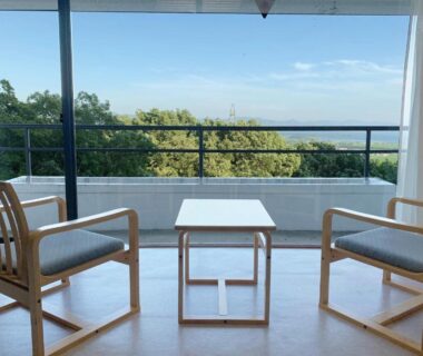Two wooden chairs and table on balcony at Villa Inawashiro, overlooking treetops in Fukushima Tōhoku