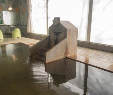 Indoor tiled onsen with wooden water spout and washing area at Villa Inawashiro, Fukushima
