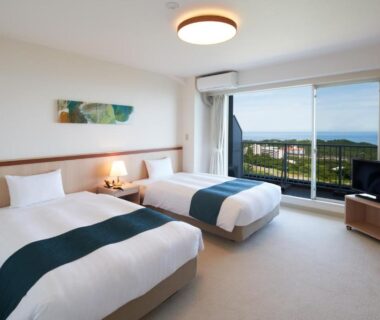Twin beds with balcony overlooking distant sea and green hills at Village Izukogen, Shizuoka