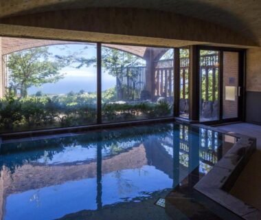 Indoor onsen bath with large window overlooking coastal view at Village Izukogen Shizuoka