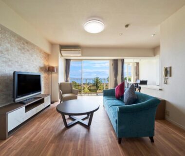 Bright living area with teal sofa, TV and balcony at Village Izukogen in Shizuoka