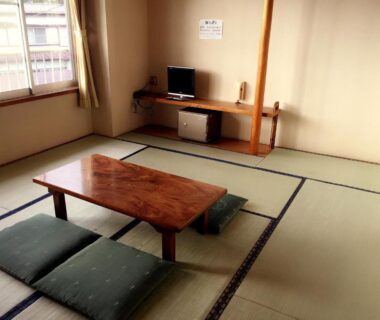 Tatami room with low wooden table, floor cushions, television and window at Village Sun Lake Kawaguchiko Yamanashi