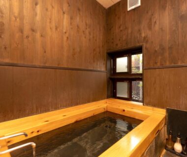 Indoor wooden soaking tub with wood-paneled walls and small window at Wa no Yado Sagiritei Ōita