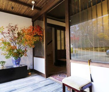 Ryokan entrance with seasonal flower arrangement, shoji door, wooden floor and window overlooking roadside umbrella
