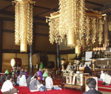 Guests seated on red carpet inside ornate temple with golden hanging ornaments, Wakamatsu Honten, Chiba