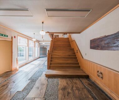 Entrance lobby with wooden staircase, stone inlay flooring and wood paneling at Wakamatsu Hot Spring Resort, Hokkaidō