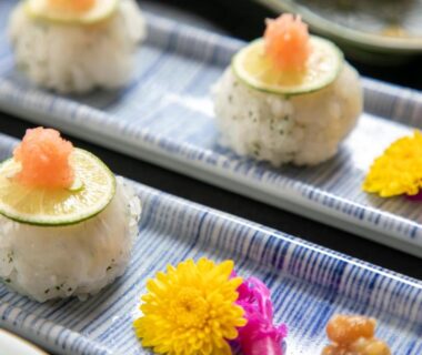Small rice balls topped with thin citrus slice and grated garnish on ceramic platter with edible flowers