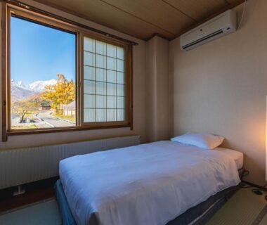 Single bed on tatami floor with shoji window framing autumn mountains outside Hakuba Nagano