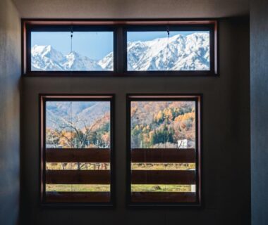 Framed snow-capped peaks and autumn trees seen from wooden windows at Wakata Lodge Hakuba, Nagano