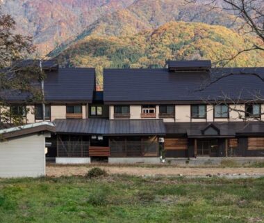 Multi-building ryokan exterior at Wakata Lodge Hakuba with wooden facades and mountain backdrop in Nagano
