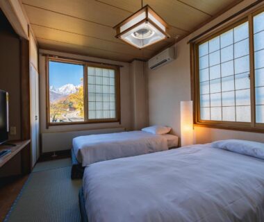Twin beds on tatami with shoji screens and mountain view through window at Wakata Lodge Hakuba Nagano