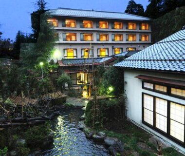 Lit multi-storey ryokan beside a flowing stream and landscaped garden in Niigata, Chūbu