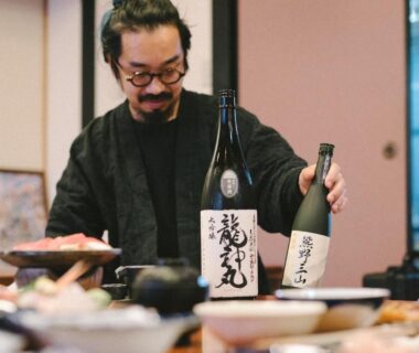 Staff pouring sake with bottles on low table and assorted dishes in a ryokan dining room, Wakatake, Wakayama
