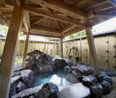 Covered rock outdoor bath with wooden shelter and bamboo fence at Wakatake, Niigata