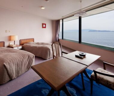 Twin bedroom with low table and large window overlooking coastal waters at Wakayama Kada Kaigetsu