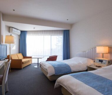 Spacious twin room with seating area, desk, lamps and large window at Wan Wan Paradise Izukogen, Shizuoka