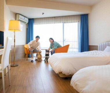 Twin beds, low table with two people, wood floor and balcony at Wan Wan Paradise Izukogen