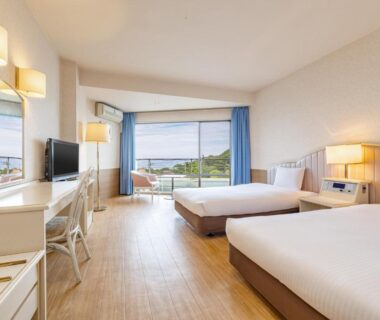 Bright twin room with balcony, two beds, desk and landscape view at Wan Wan Paradise Izukogen Shizuoka
