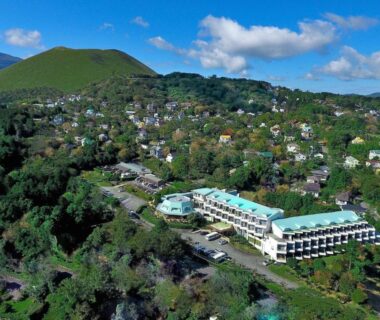 Aerial view of the resort building on a green hillside near houses at Wan Wan Paradise Izukogen, Shizuoka, Japan