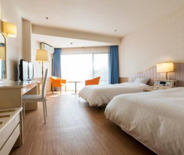 Spacious western-style twin room with wooden floor, two beds, desk, balcony and seating at Wan Wan Paradise Izukogen Shizuoka
