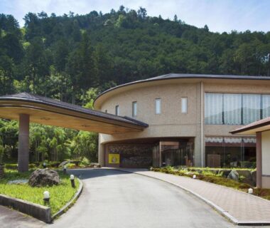 Driveway and curved entrance canopy of Wan Wan Paradise Matsusaka with hillside forest backdrop in Mie, Kansai
