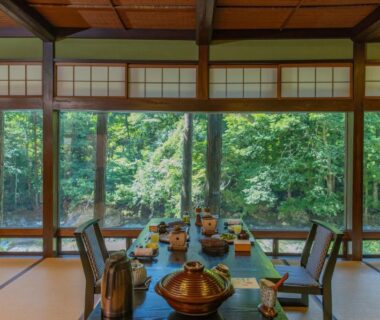 Tatami room with low dining table, teapots and shoji screens overlooking forest at Wanosato, Gifu