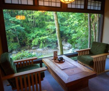 Traditional tatami room with low wooden table and chairs overlooking a lush garden with trees and stones